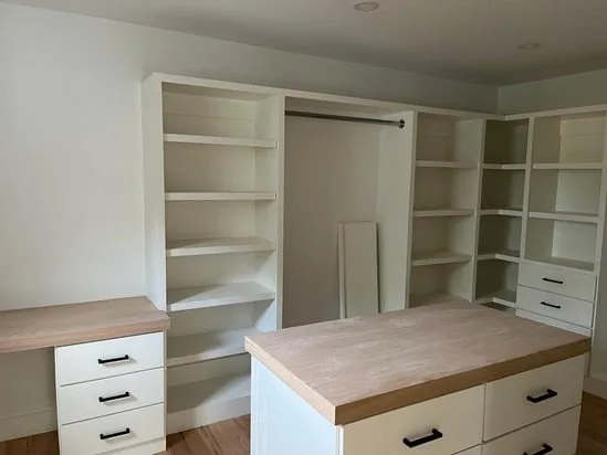 Custom walk-in closet carpentry with wood-top island and organized shelving.